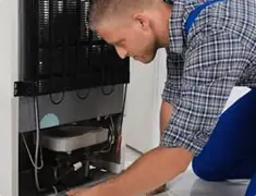 Refrigerator repair technician servicing the compressor and condenser area in Bradenton, FL